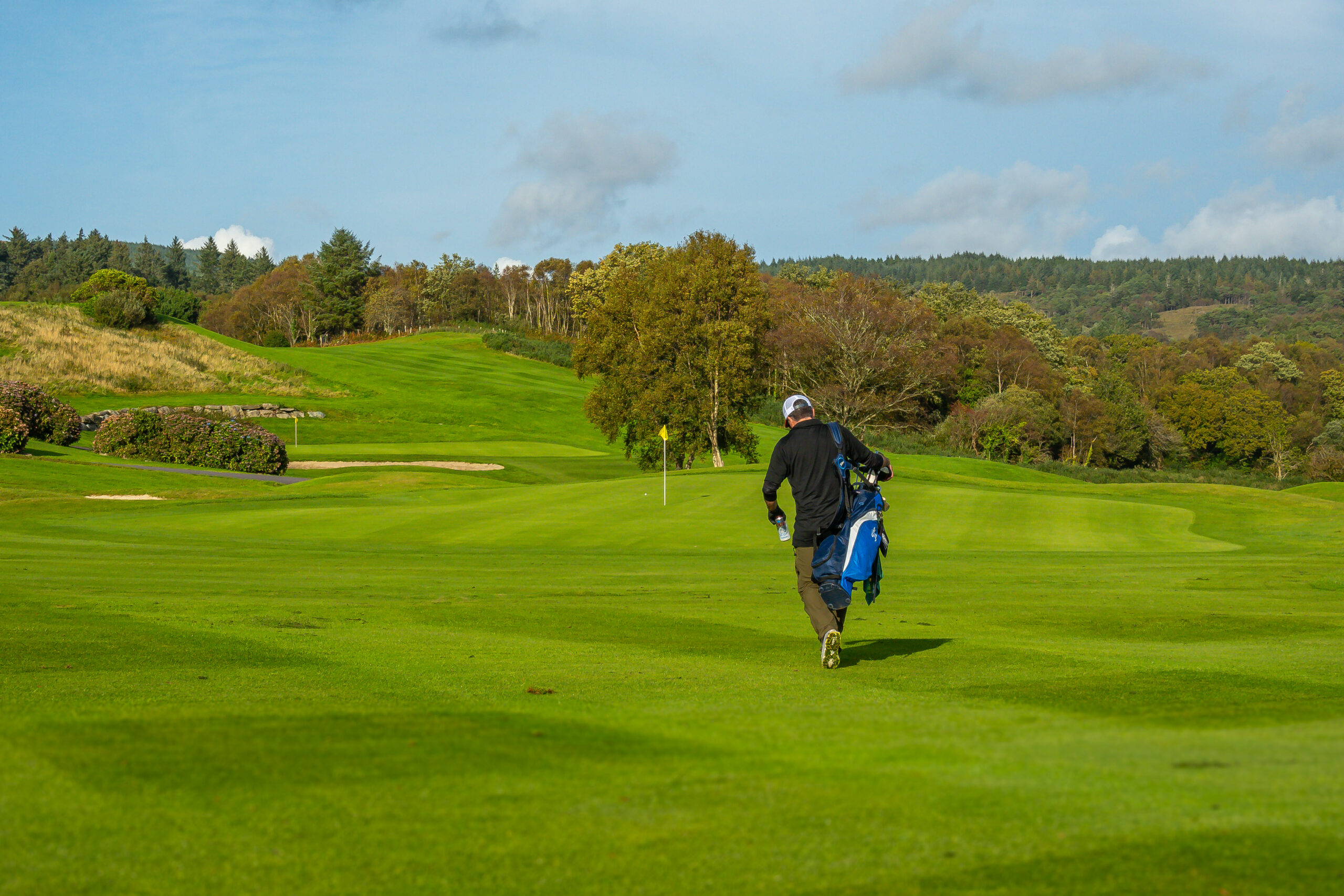 Golfer carrying a bag across a parkland course in Ireland