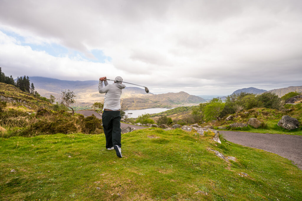 Golfer teeing off above a lake and mountain landscape in Ireland