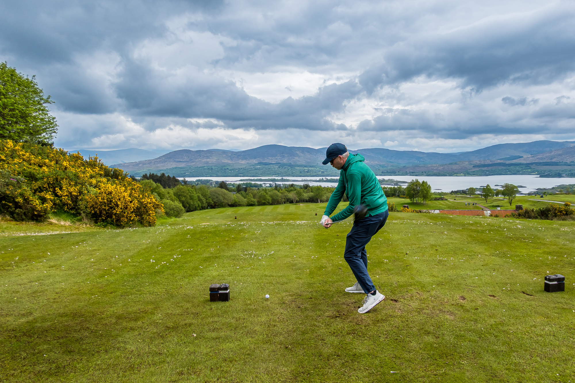 Golfer teeing off above a lake and mountain landscape in Ireland