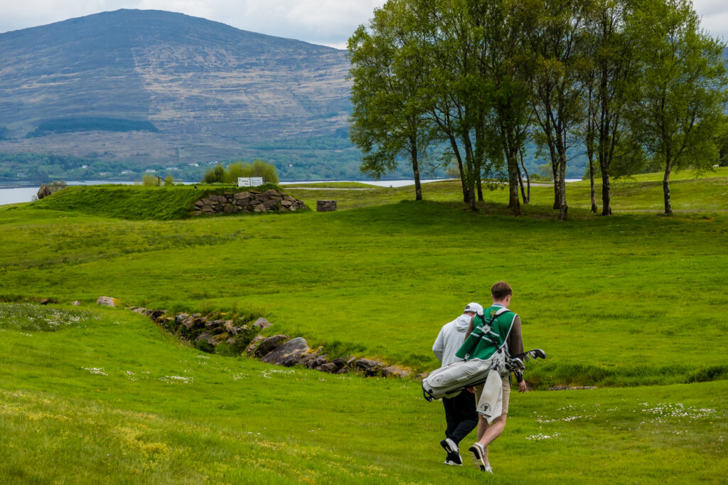 A caddie walking an Irish golf course beside mountains and water