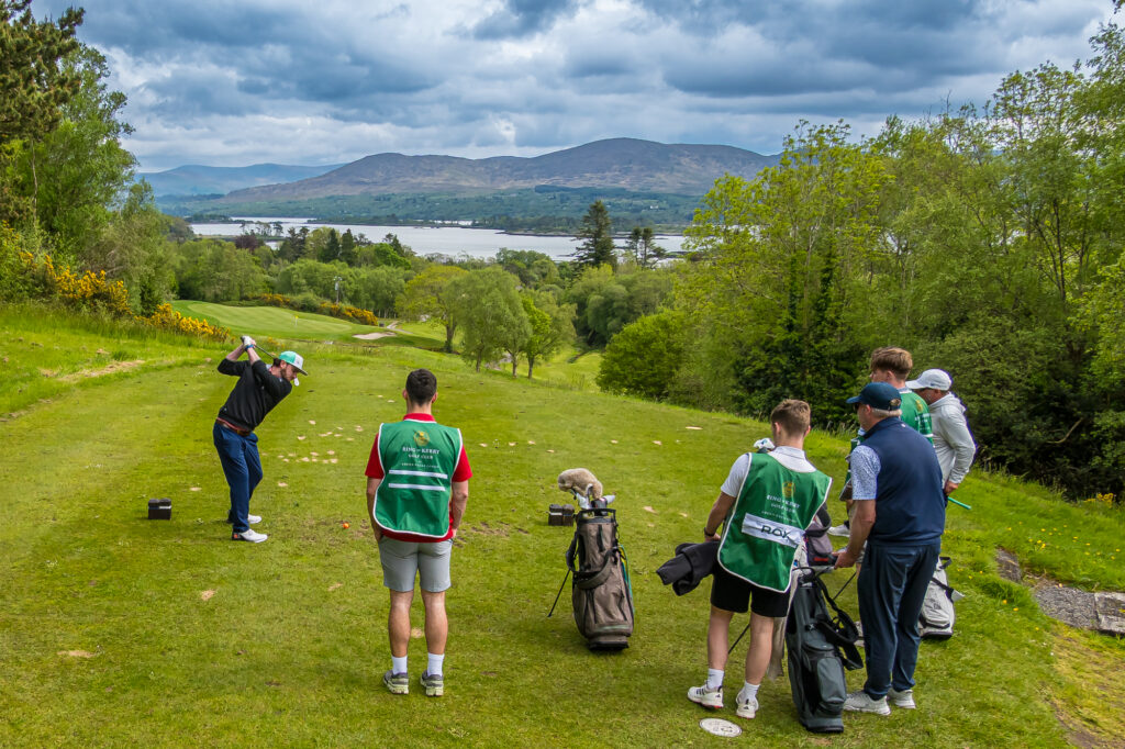 Golfers and caddies preparing to play from a scenic Irish tee box
