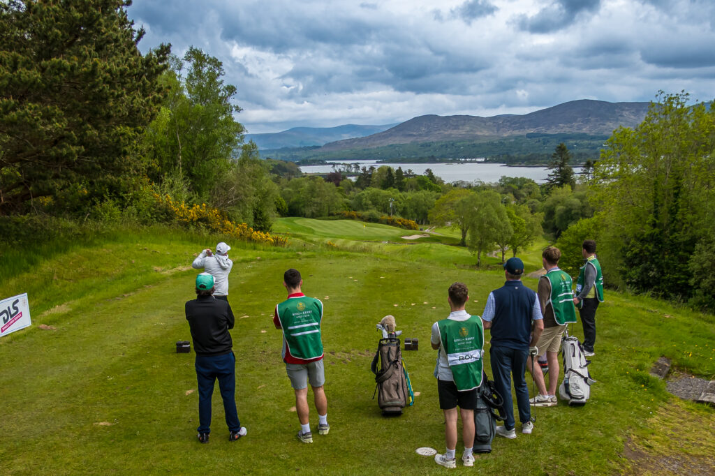 Golfers and caddies overlooking an Irish golf course and mountain lake