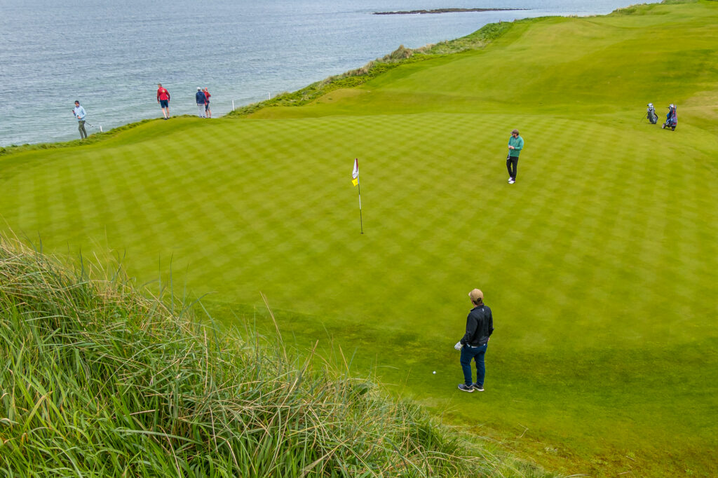 Golfers play a seaside green on a bright Irish links course