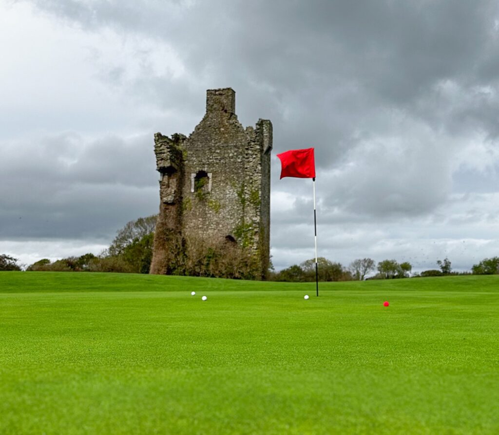 Castle ruins and red golf flag beside a green in County Kerry, Ireland