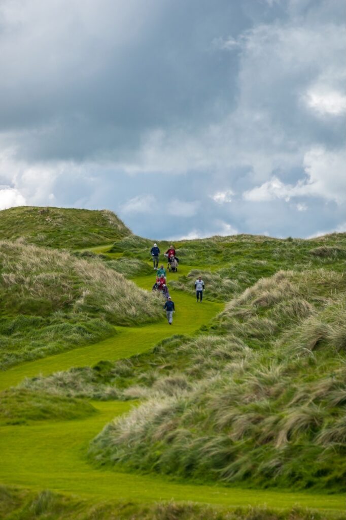 Golfers walking through towering links dunes on an Irish golf course
