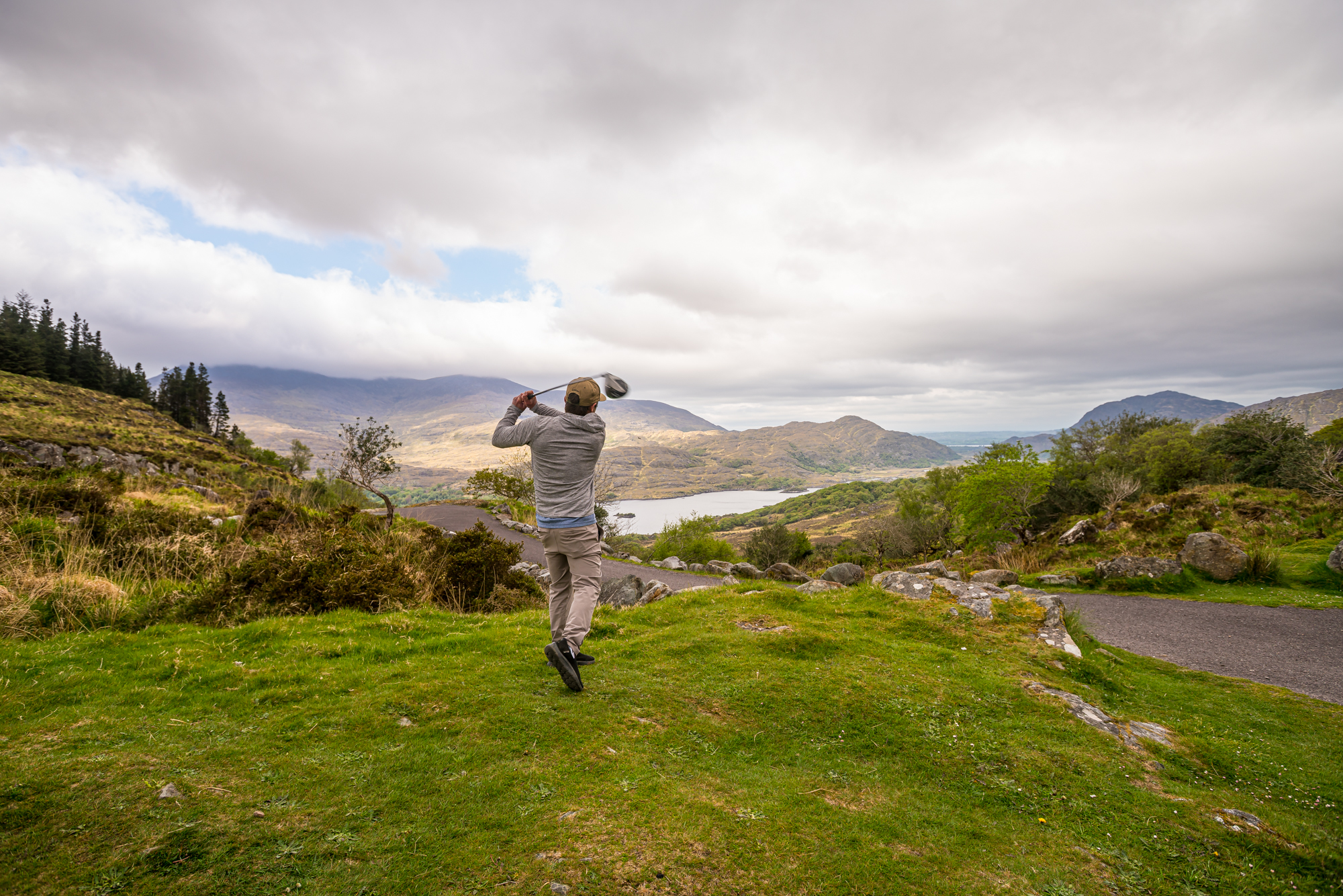 Ben Siegel finishing a golf swing above a lake and mountain landscape in Ireland during the May 2026 Golf Nomad trip