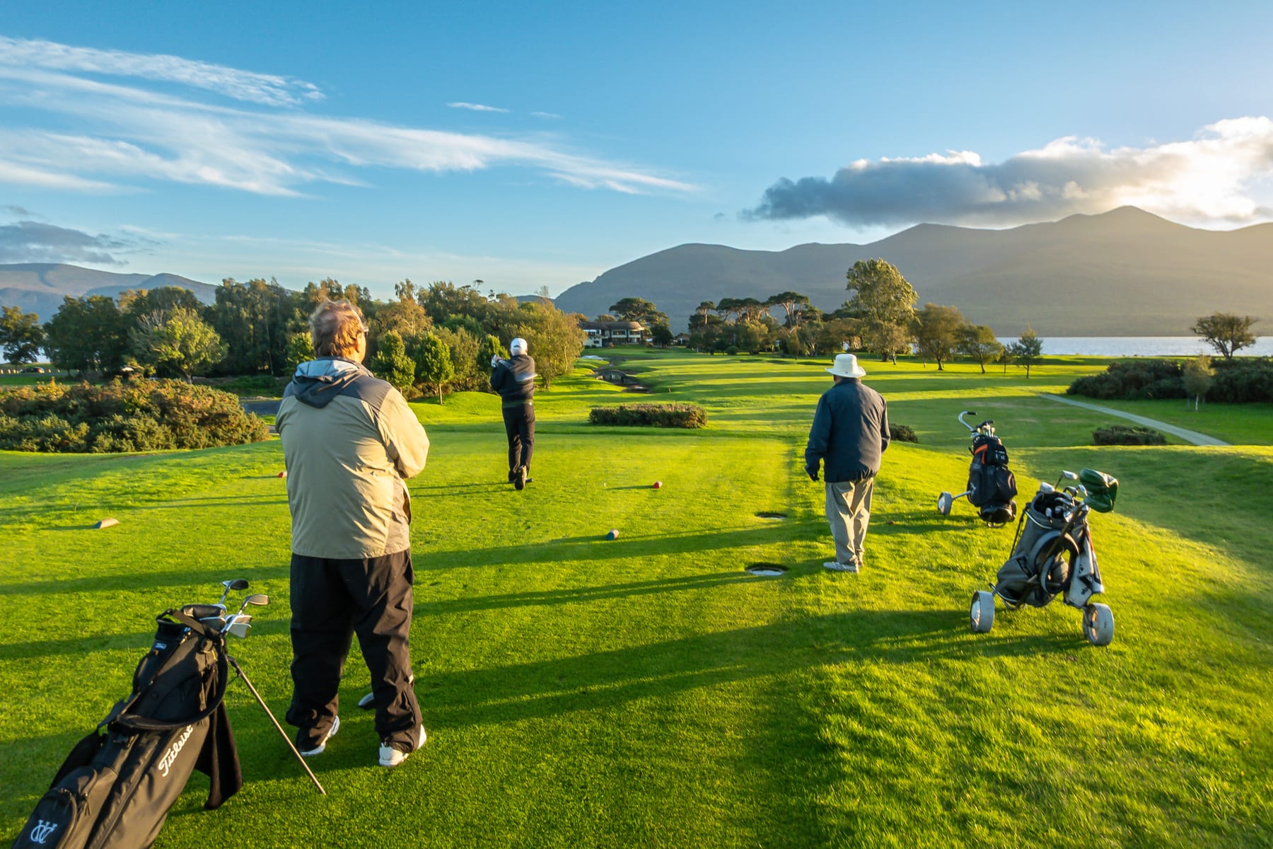 Golfers on a sunlit green with mountains and water behind them during the Ireland trip
