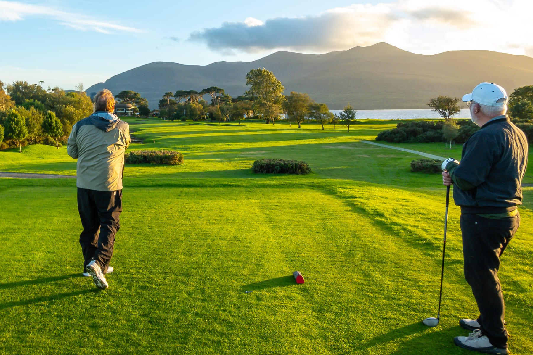 Golfers beside a tee with an evening view across the lake and mountains