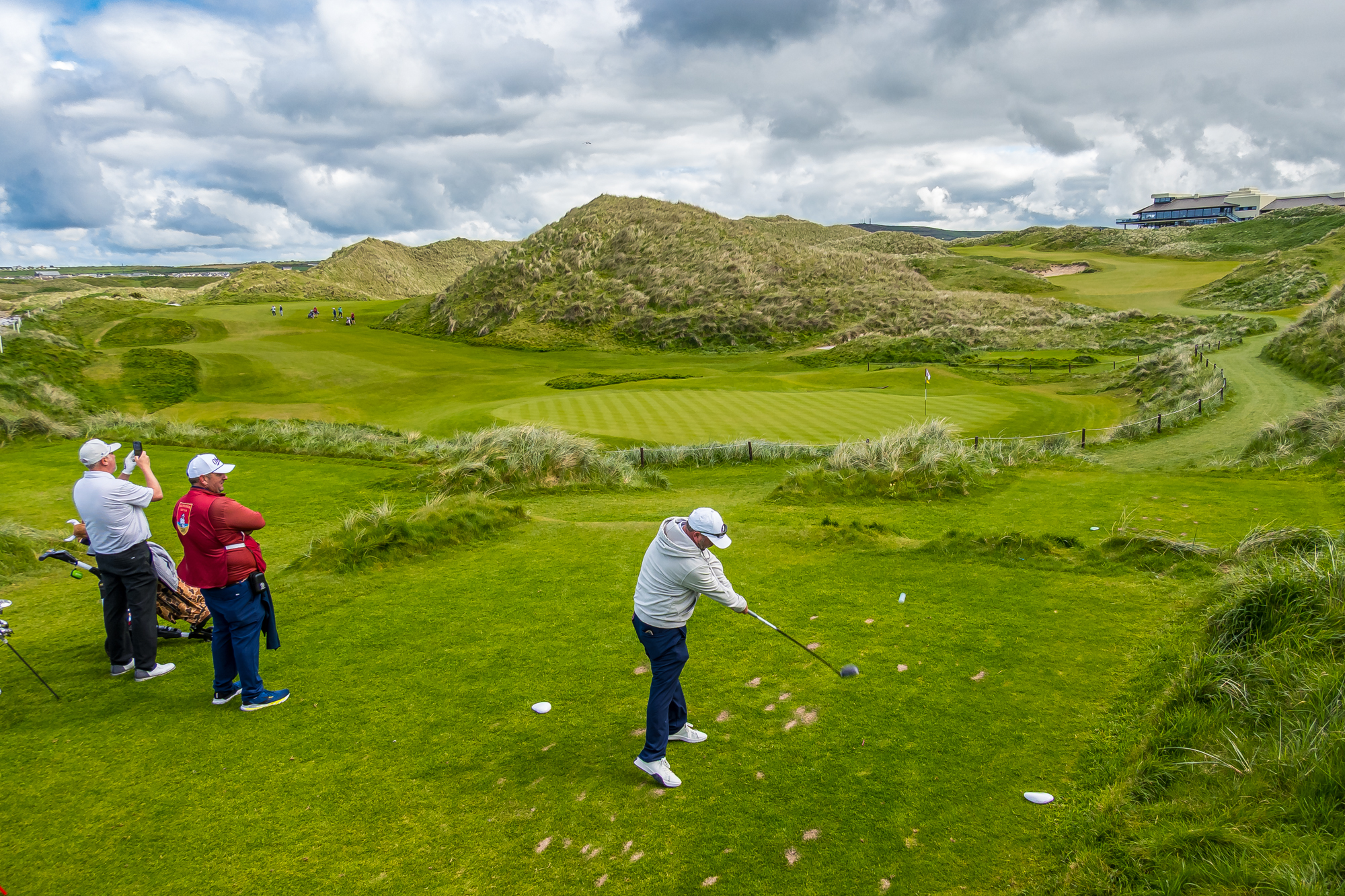 Golfer teeing off on an Irish links course surrounded by grass-covered dunes